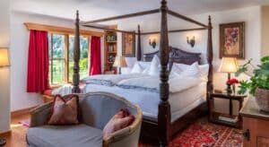 Luxrious bedroom with mahogany four poster bed, loveseat, large window with red curtains