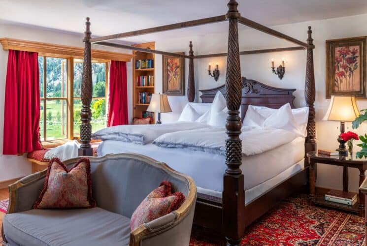 Luxrious bedroom with mahogany four poster bed, loveseat, large window with red curtains