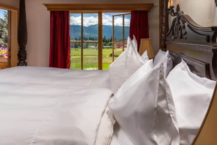 King four poster bed in plush white linens in front of large windows overlooking mountains