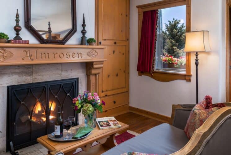 Sitting area in a bedroom with a loveseat and table in front of a fireplace with a decorative mantle with a name engraved in it