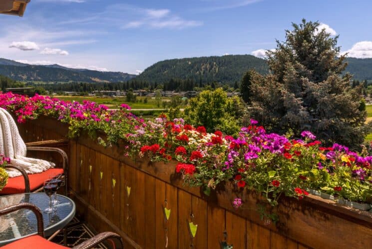 Outdoor balcony with flowers lining the railing, patio chairs and table, overlooking an expansive valley and mountain range