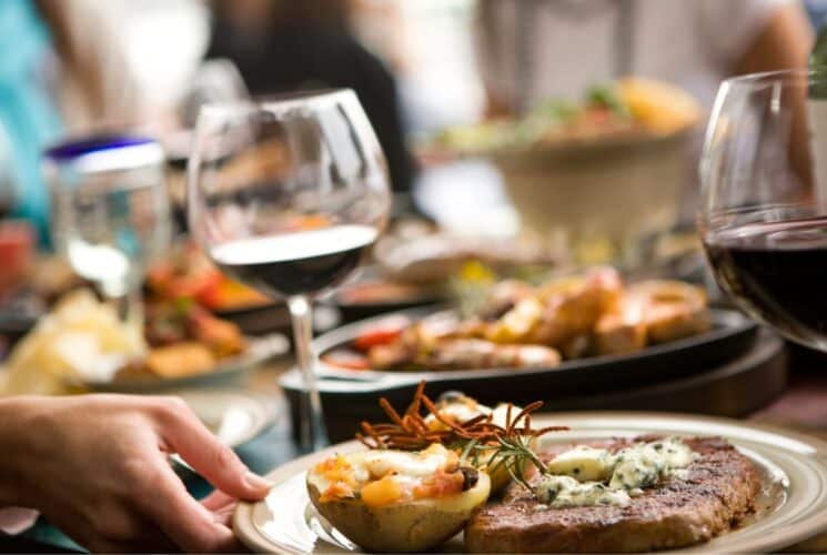 A restaurant table filled with plates of food, wine glasses and blurred people at the table