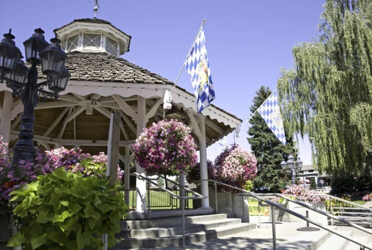 Large white gazebo surrounded by trees, hanging flower baskets next to a lawn