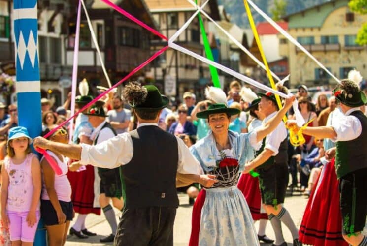 Festival in a town square with people in colorful German costumes dancing with ribbons