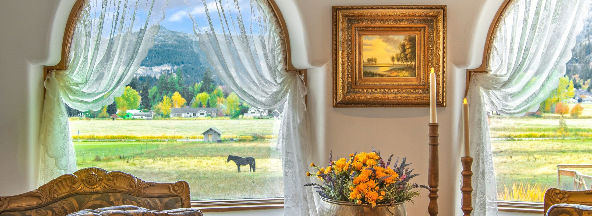 Sitting area with two plush decorative chairs and table in front of large arched windows overlooking a valley and mountains