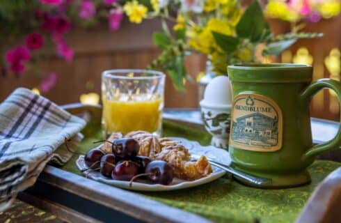 Wood tray with plate of cherries and a pastry, green ceramic mug, glass of orange juice and a hard boiled egg