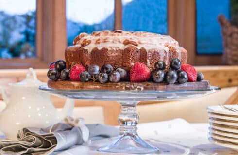 Delicious and golden brown freshly baked bundt cake on a glass platter with berries and grapes