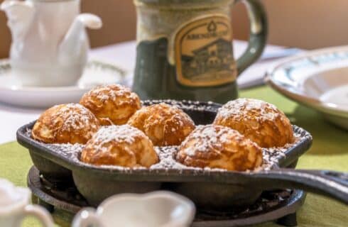 Cast iron pan with freshly baked popovers dusted in powdered sugar on a table with green and white linens