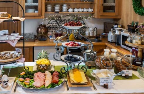 Kitchen counter full of a variety of serving platters with pastries, meats and cheeses, fruit, yogurt and granola