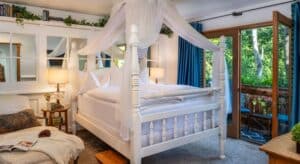 Cozy bedroom with canopy bed, wall of mirrors, chaise lounge, blue curtains, door open to patio