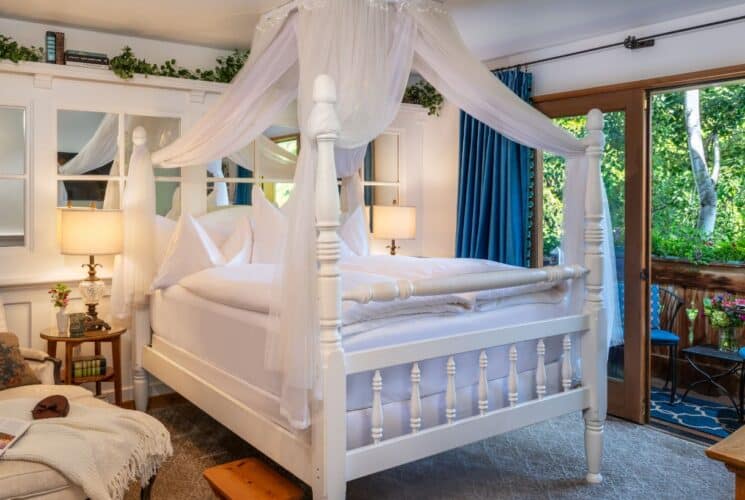 Cozy bedroom with canopy bed, wall of mirrors, chaise lounge, blue curtains, door open to patio