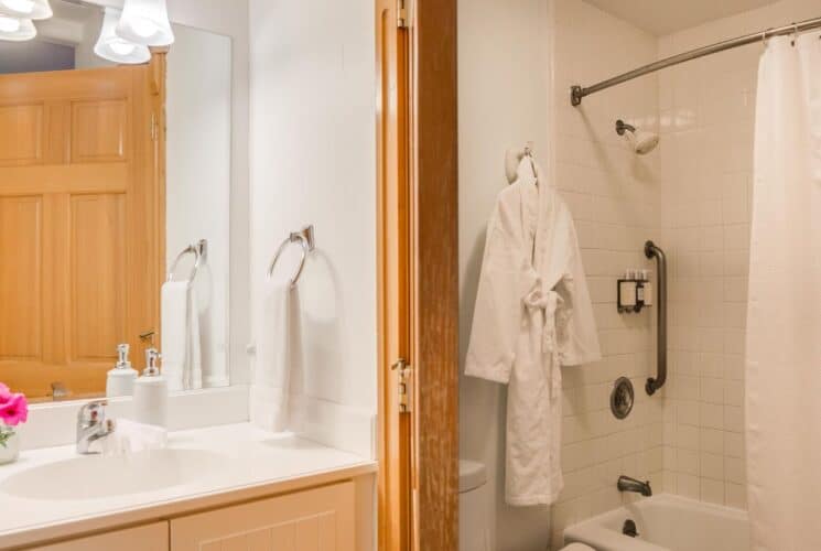 Bathroom with white tiled stand up shower, hanging robe, vanity with single sink and large mirror