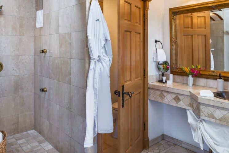 Elegant bathroom with tiled shower, vanity with copper sink and large framed mirror, plush white robe hanging on a hook