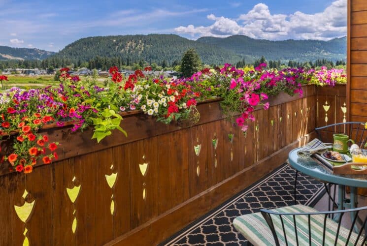 Second story outdoor patio with flowers lining the railing, patio chairs and table, all overlooking an expansive valley and mountains