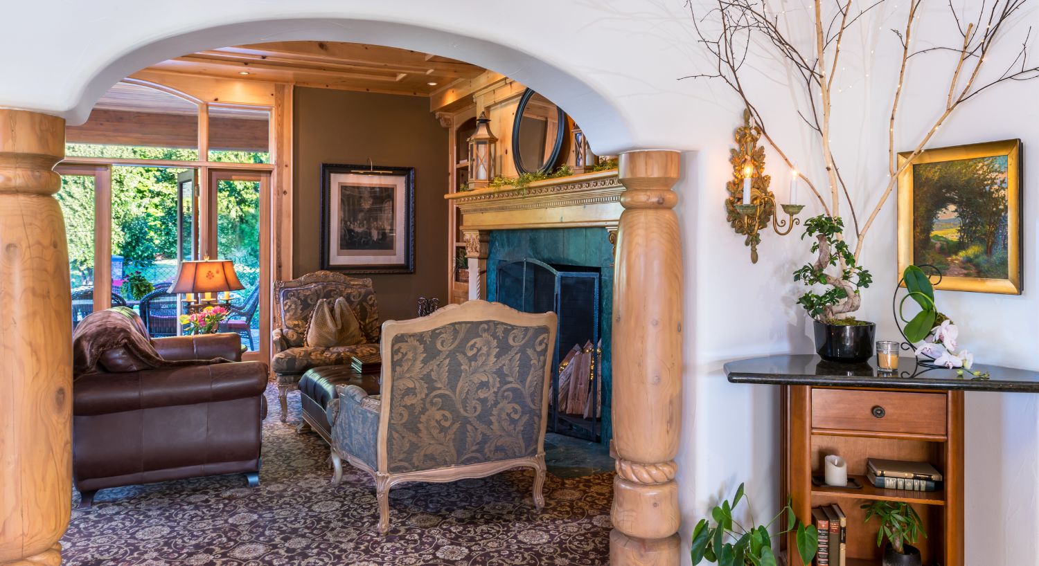 Arched doorway with wood column detail looking into a formal living room with a large fireplace and glass doors open to a patio