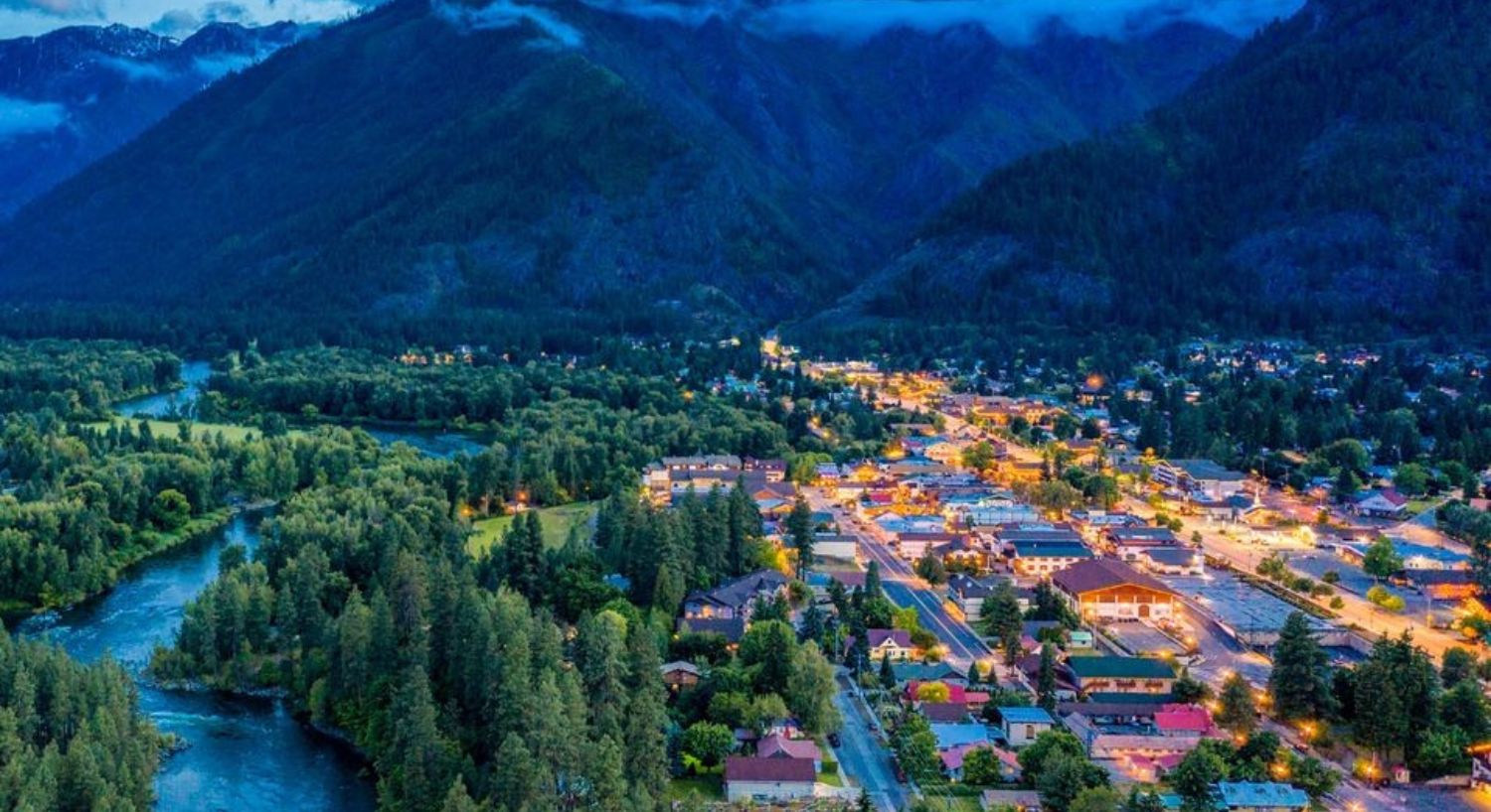 Aerial view of a small town lit up at night at the base of a large mountain range and next to a river