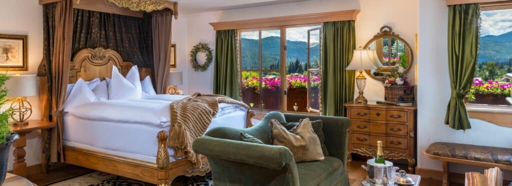 Luxury bedroom with ornate king bed, plush green loveseat, antique furniture, glass doors to an outdoor patio overlooking the mountains