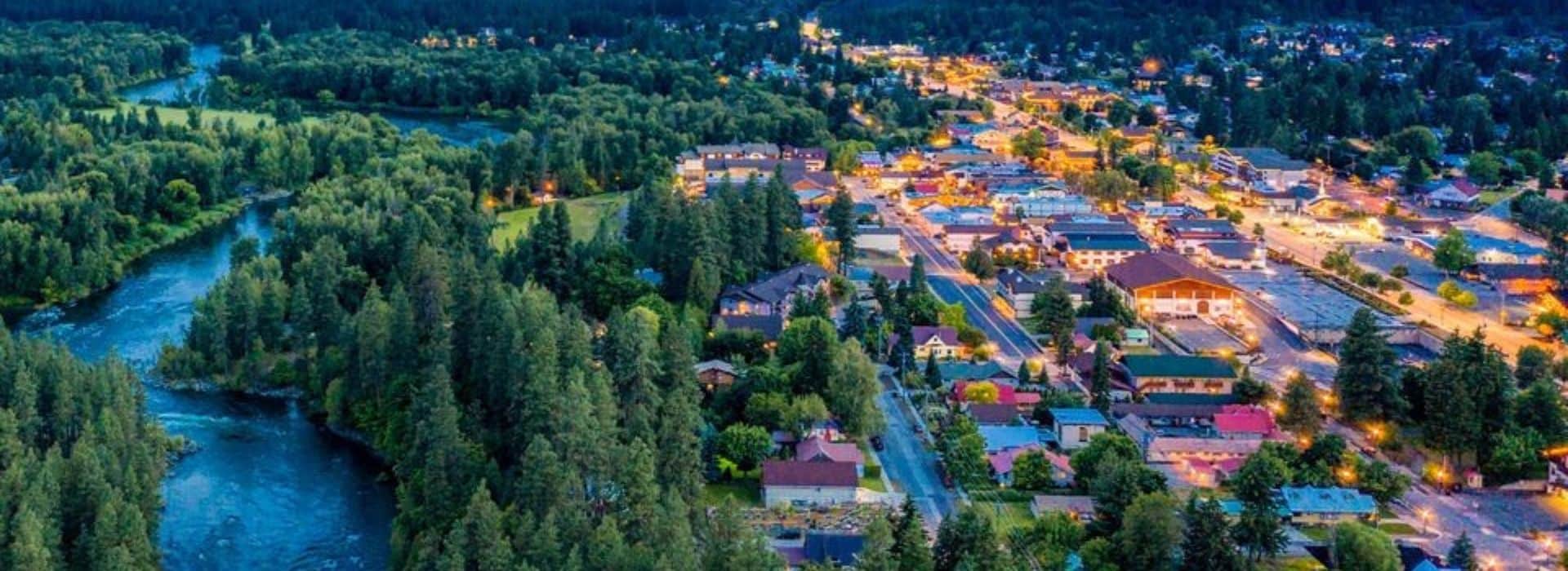 Aerial view of a small town lit up at night, nestled at the base of an expansive mountain range and next to a river