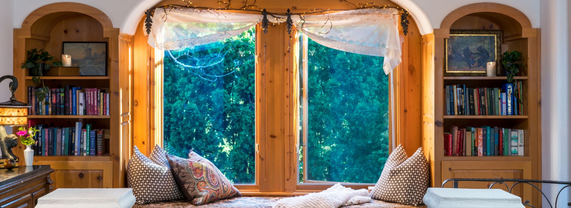 Window seat with throw pillows by a large window, flanked by two arched built in bookshelves