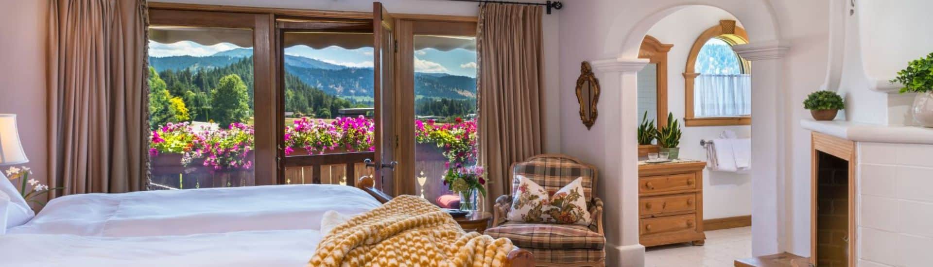 Elegant and bright bedroom with bed in front of a large patio door and windows overlooking mountains, arched doorway into a bathroom