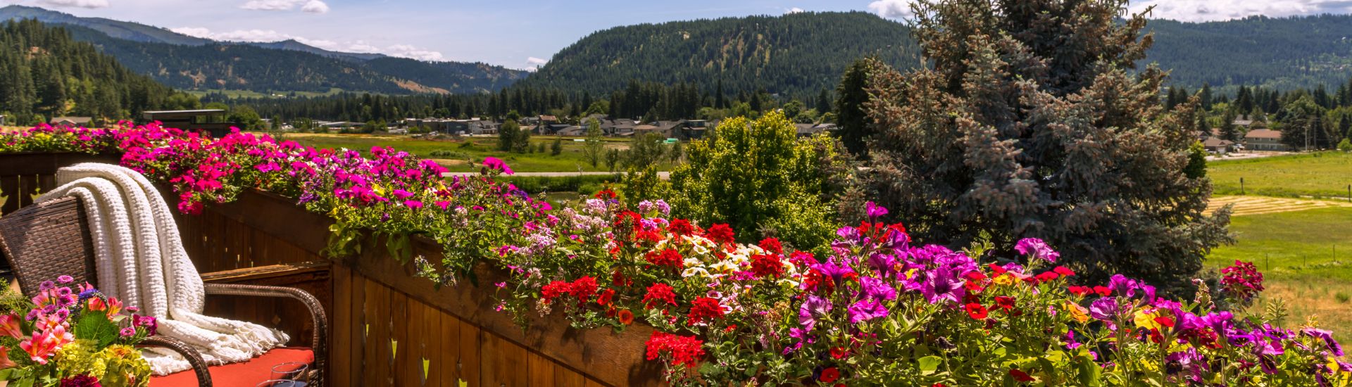 Second floor balcony lined with flowers, chair with a throw blanket, overlooking an expansive valley and mountain range