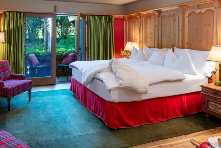 Cozy bedroom with king bed, wood paneling feature, plaid sitting chairs and door open to a patio