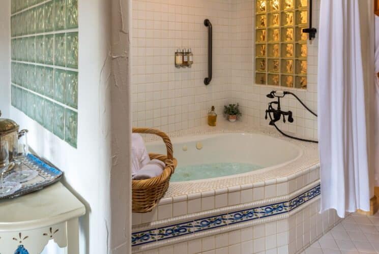 Large jacuzzi tub with decorative tile detail, glass block walls, hanging white robe