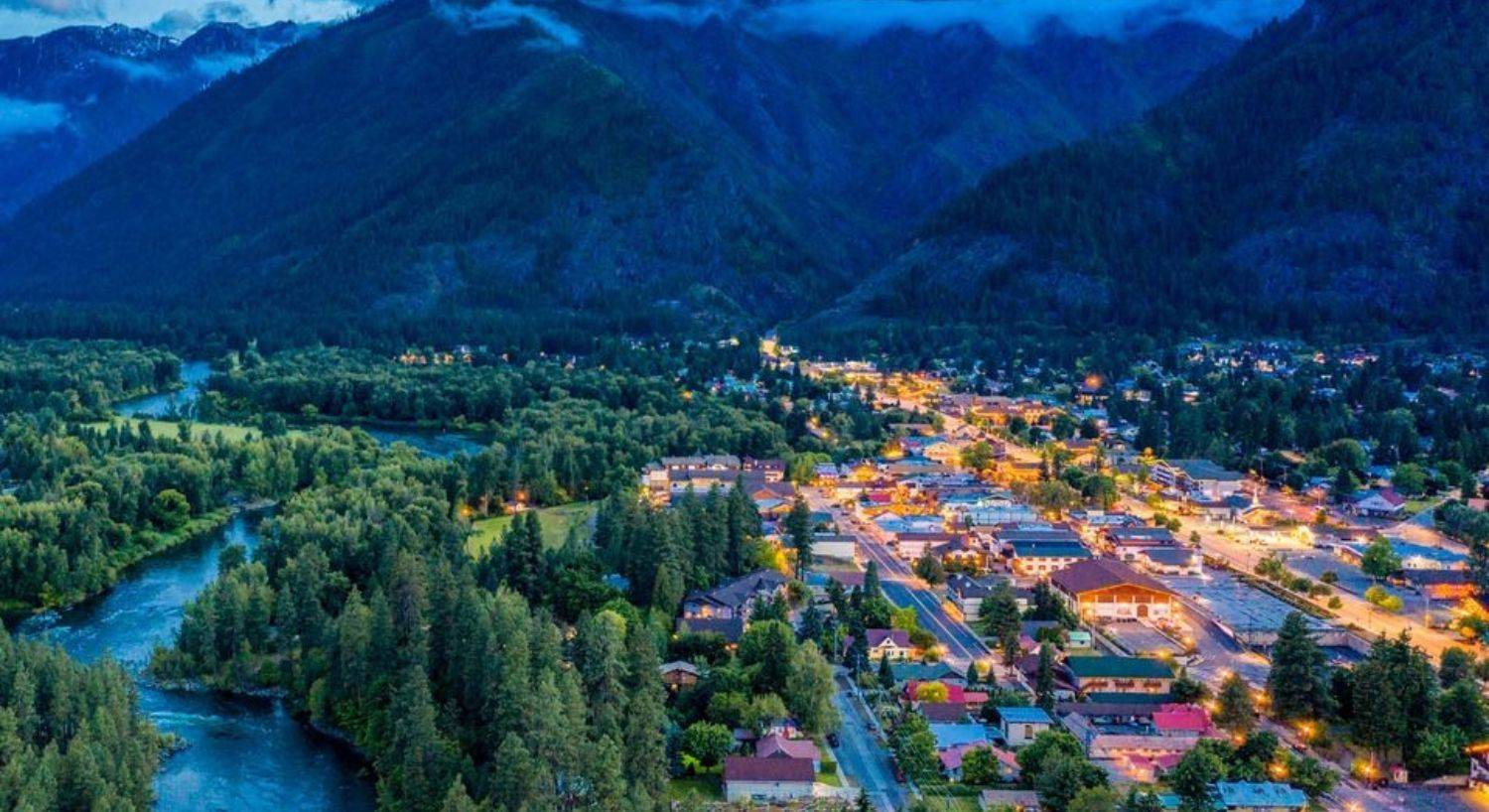 Aerial view of a small town lit up at night at the base of a large mountain range and next to a river