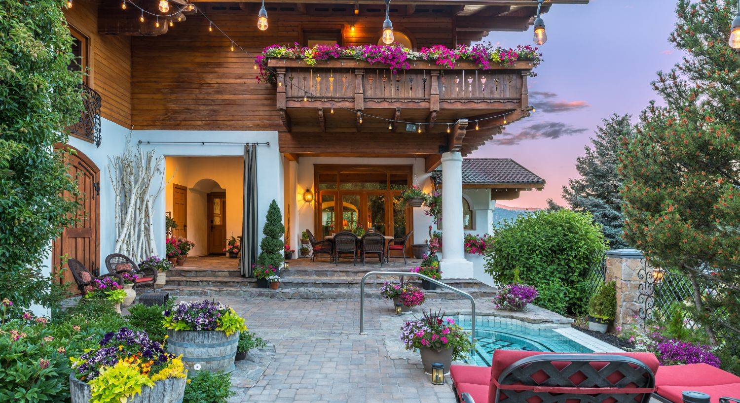 Outdoor patio of a luxury two story white and brown villa with hot tub, patio and lounging chairs, and colorful flower pots