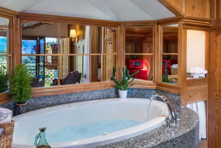 Large oval soaker jacuzzi tub with a wall of mirrors reflecting a patio door to the outdoors